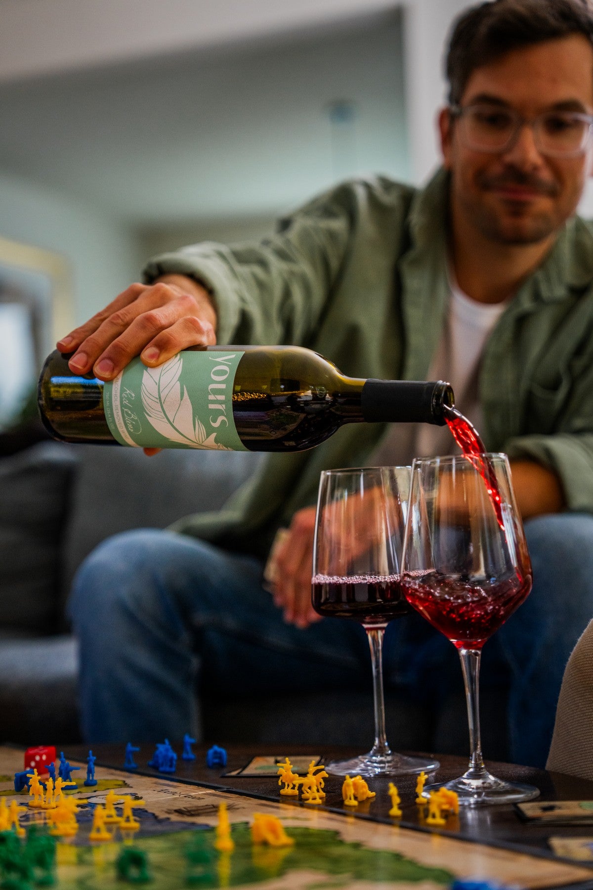 Man pouring YOURS non-alcoholic red wine into two glasses over a board game