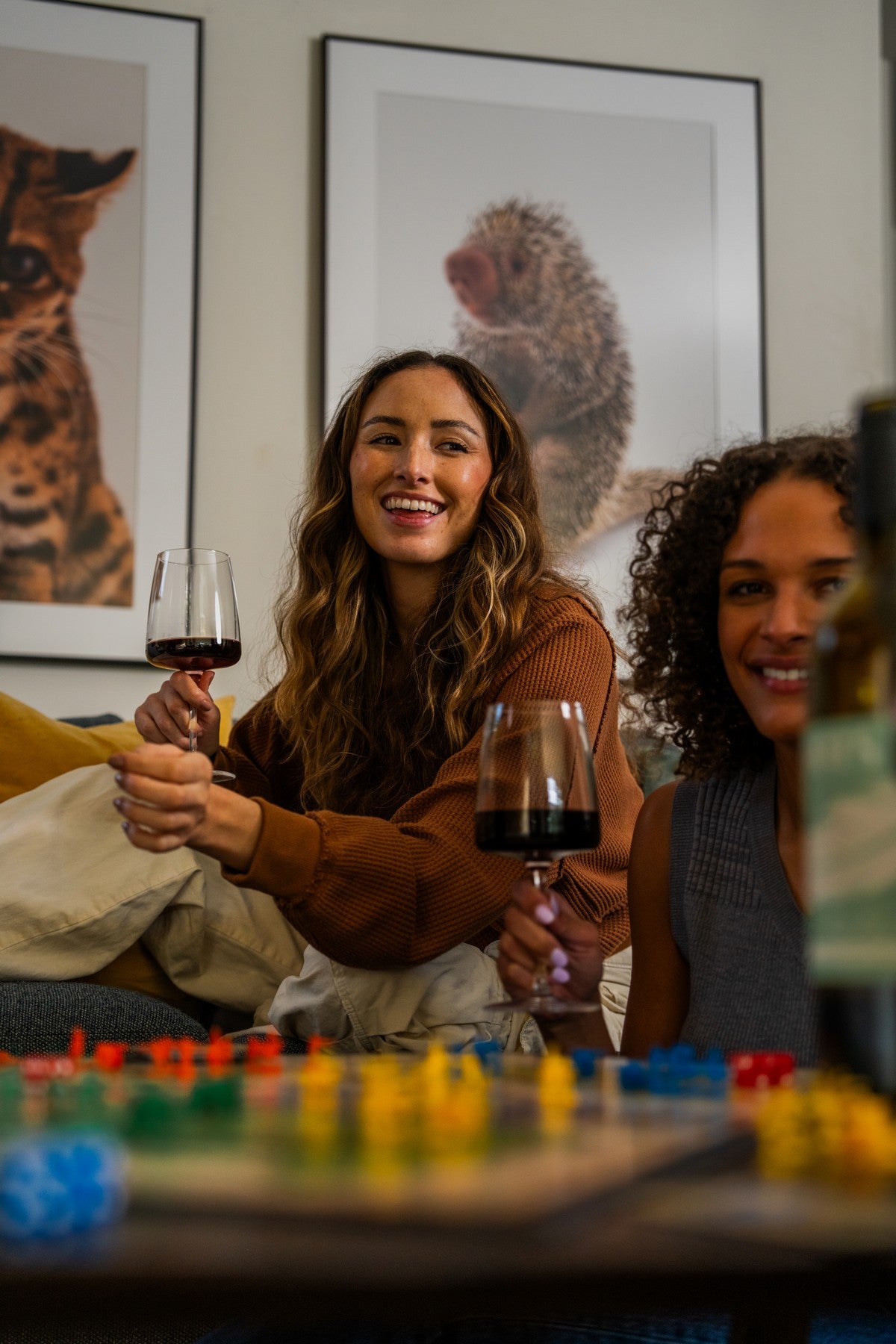 Two women holding glasses of YOURS non-alcoholic red wine at a table with a board game