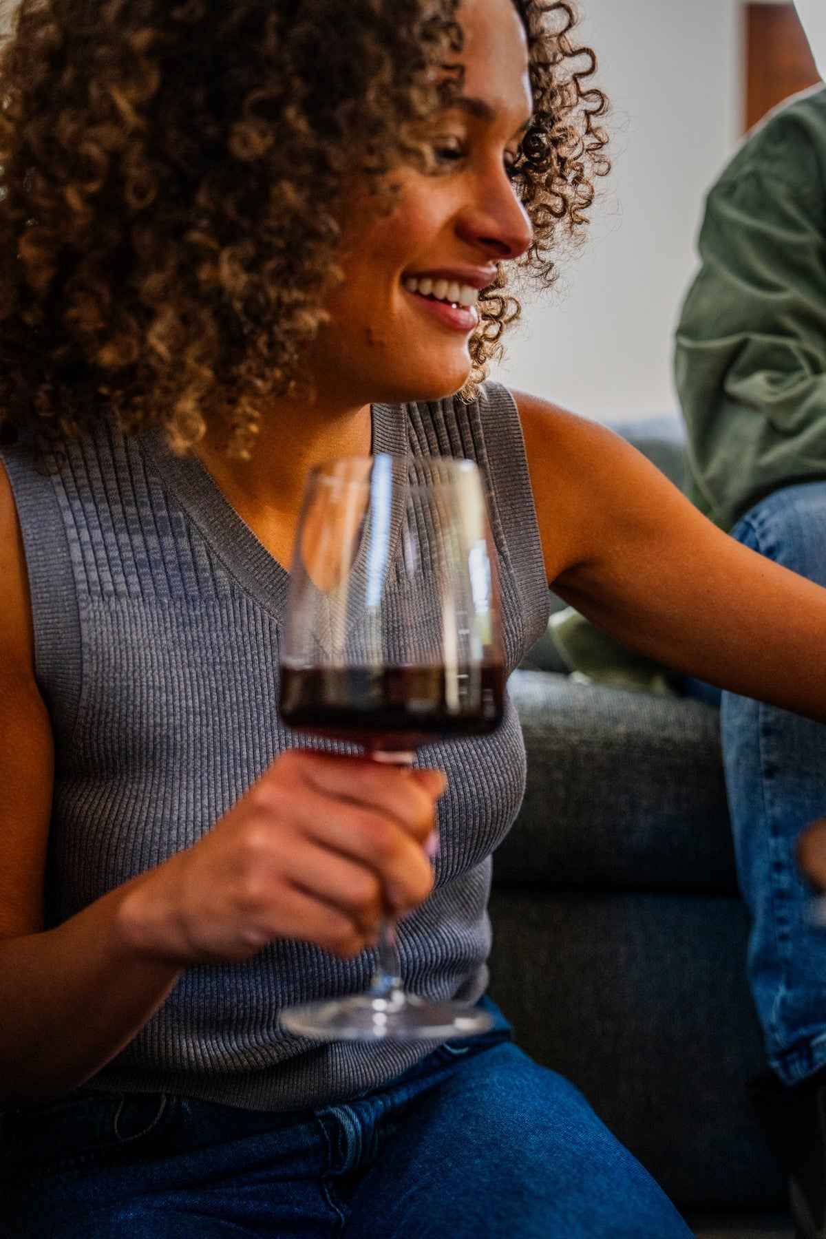 Woman sitting on a sofa holding a glass of YOURS non-alcoholic red wine and smiling